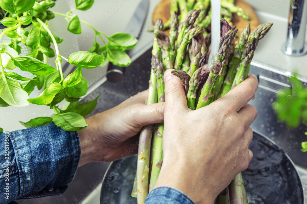 cropped shot of male hands in soil washing fresh asparagus in kitchen sink.