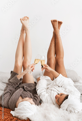 Relaxed girlfriends laying with legs up and drinking champagne © Prostock-studio