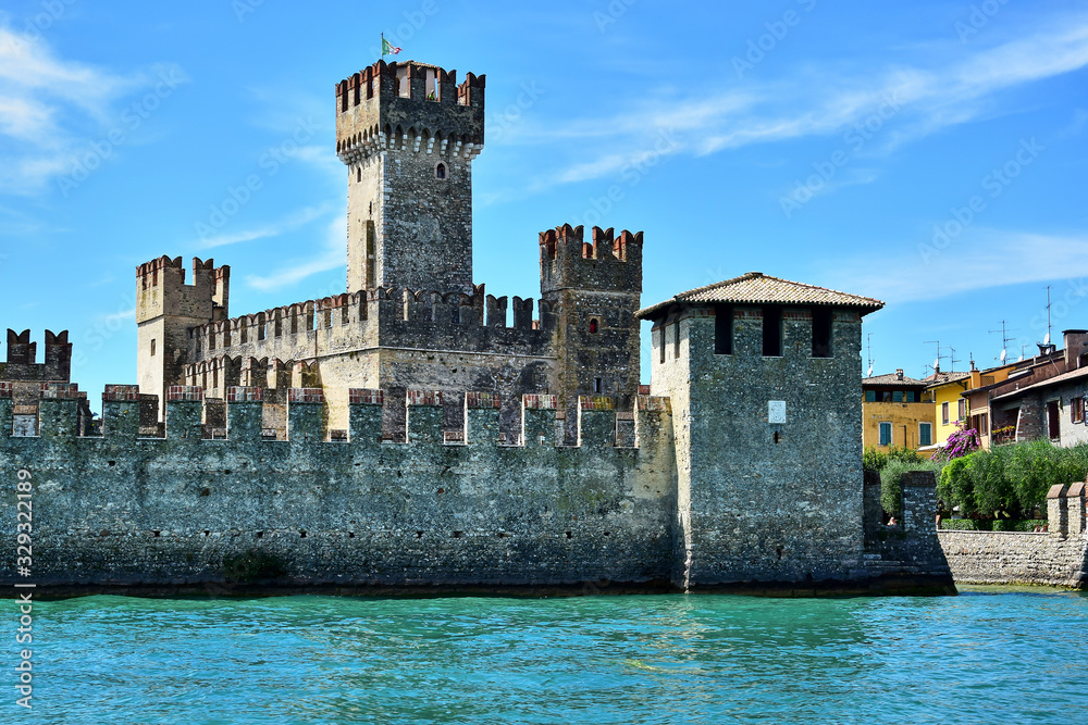 Sirmione / Lombardy, Italy - Castello Scaligero fortress, stands on the shores of Lake Garda, turquoise water in front of the fortress, blue sky with white clouds, in the summer afternoon.