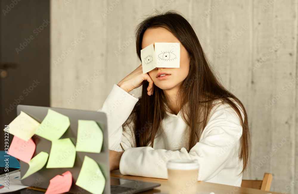 Tired freelancer sleeping at workplace with stickers on eyes Tired freelancer sleeping at workplace with stickers on eyes