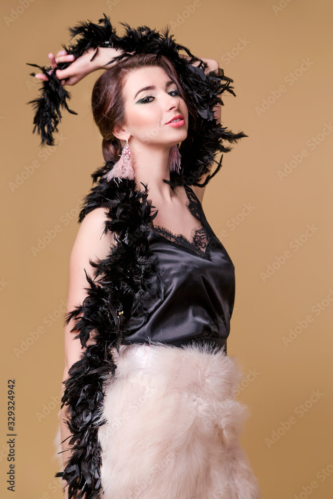 Fototapeta premium Brunette beautiful woman in black boa from ostrich feathers is dancing on beige background