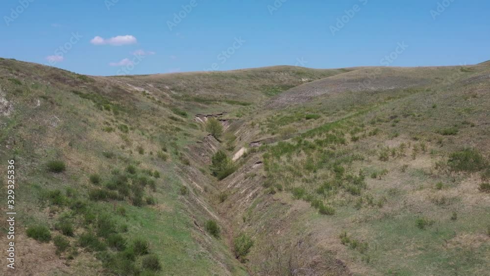Flying over ravine between hills with blue sky Flying over ravine between hills with blue sky