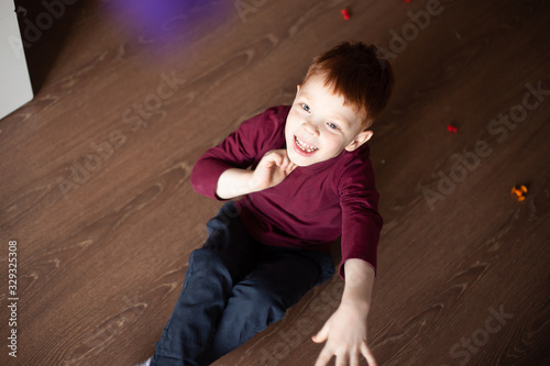 cute, smiling red-haired boy in a multi-colored sweater plays in the constructor