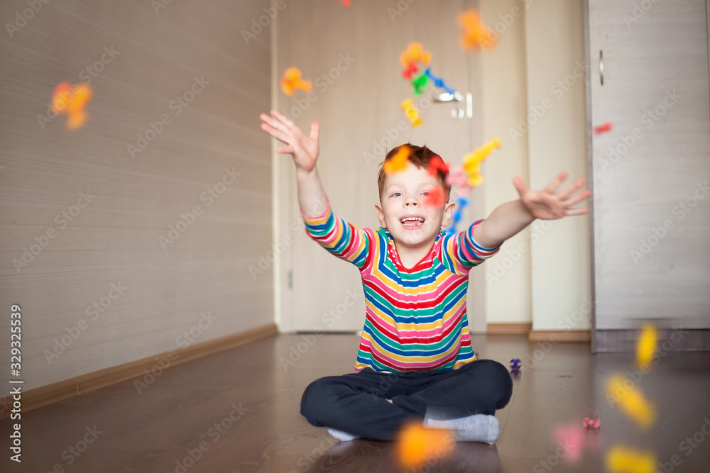 Fototapeta premium a cute, smiling red-haired boy in a multi-colored sweater plays a constructor, throws up and throws details