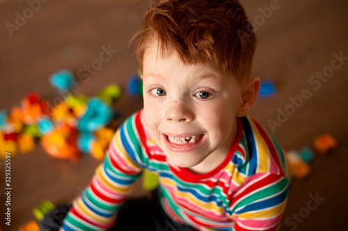 red-haired boy in a multi-colored jacket holds plays in the constructor blocks