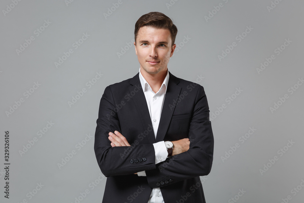 Smiling young business man in classic black suit shirt posing isolated on grey wall background studio portrait. Achievement career wealth business concept. Mock up copy space. Holding hands crossed. Smiling young business man in classic black suit shirt posing isolated on grey wall background studio portrait. Achievement career wealth business concept. Mock up copy space. Holding hands crossed.