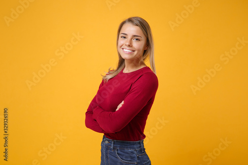 Side view of smiling young blonde woman girl in casual clothes posing isolated on yellow orange wall background studio portrait. People lifestyle concept. Mock up copy space. Holding hands crossed.