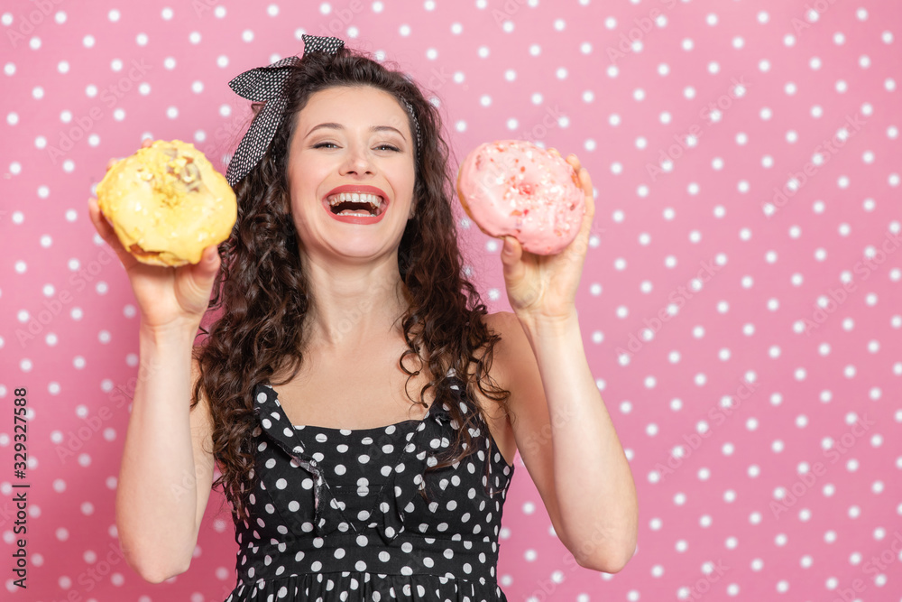 Cheerful girl is showing off two big doughnuts with yellow and pink icing and laughing delightfully. Cheerful girl is showing off two big doughnuts with yellow and pink icing and laughing delightfully.