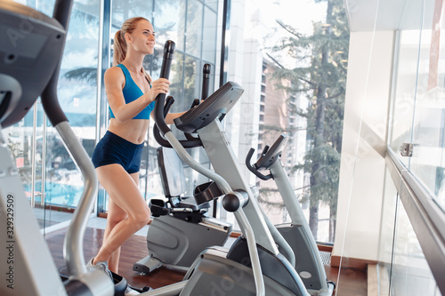 Side view of a graceful beautiful young woman fitness model is engaged with a trainer in the gym. The girl monitors her figure while exercising in the gym and eating properly