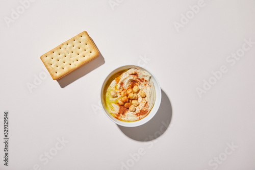 Top view of bowl with tasty hummus and crackers on grey background photo