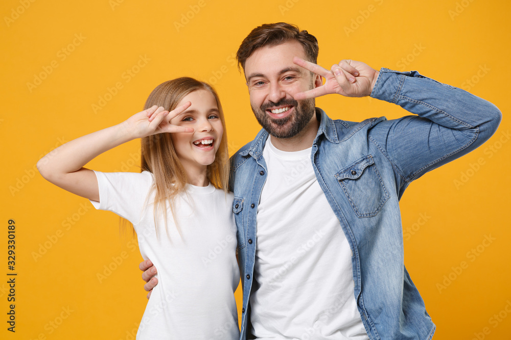 Obraz premium Cheerful bearded man in casual clothes have fun with cute child baby girl. Father little kid daughter isolated on yellow background. Love family day parenthood childhood concept. Showing victory sign.