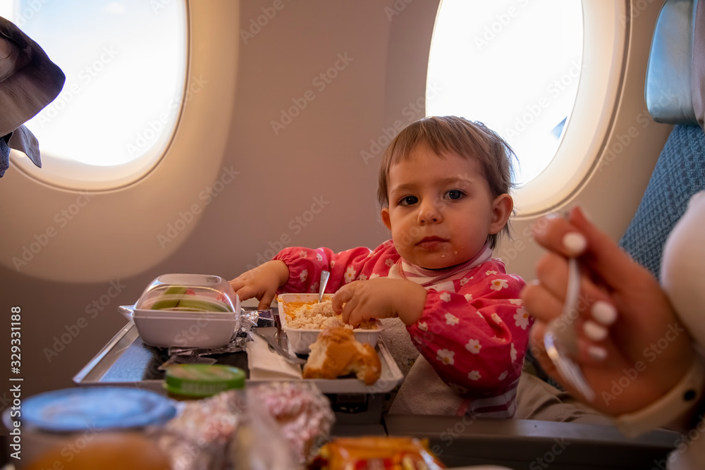young toddler passenger plane eats tasty hot special meal on board on a folding table. in the background is a window in the porthole. young toddler passenger plane eats tasty hot special meal on board on a folding table. in the background is a window in the porthole.