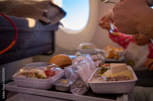 close-up passenger plane eats tasty hot meal  on board  on a folding table. in the background is a window in the porthole.