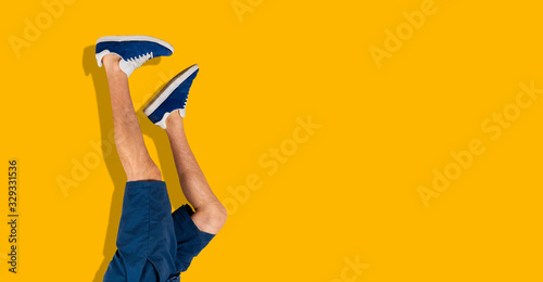 the simple human legs in sneakers upside down against the colorful wall, trendy chill and relax concept wide webn banner