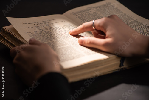 Cropped view of woman reading holy bible in dark with sunlight
