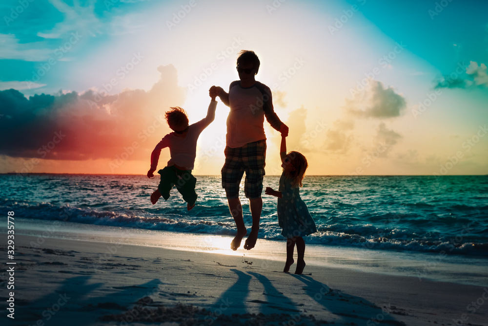 happy father with kids jumping from joy at sunset beach