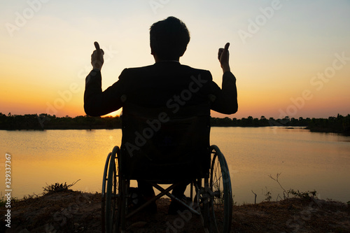 Silhouette young disabled man with river background.He is raise a hand to and sitting on wheelchair.He is looking into river.despair,lonely,hope.Photo concept depression and Patient.
