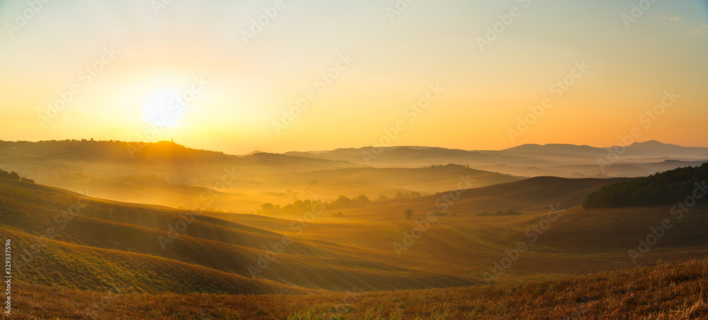 Beautiful panoramic view of orange sunset over rural landscape in Tuscany with wheat field, rolling hills, old town on horizon and rising sun. Travel destination Tuscany, Italy