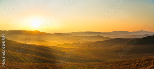 Beautiful panoramic view of orange sunset over rural landscape in Tuscany with wheat field, rolling hills, old town on horizon and rising sun. Travel destination Tuscany, Italy
