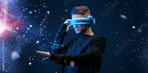 Guy using VR helmet scrolling invisible screen while interacting with virtual reality. Blue neon light. Augmented reality, future technology, game concept.
