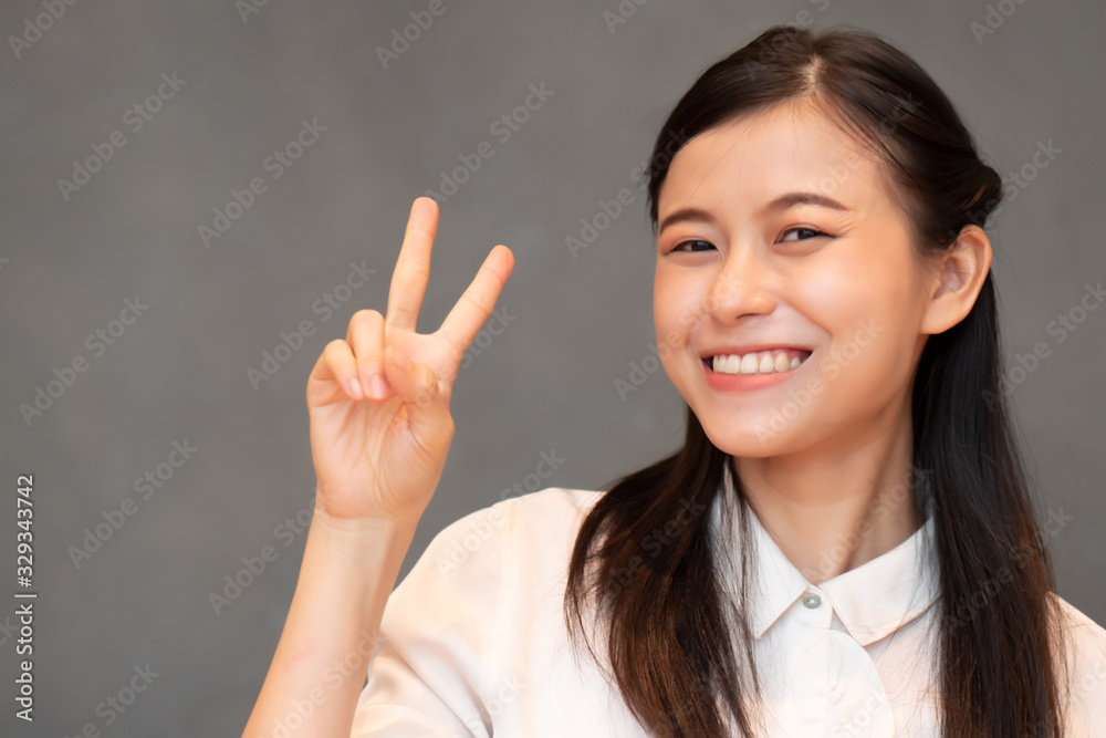 asian woman pointing two fingers; portrait of positive happy smiling southeast asian woman pointing up one finger, v for victory concept; asian Chinese adult woman model, casual theme asian woman pointing two fingers; portrait of positive happy smiling southeast asian woman pointing up one finger, v for victory concept; asian Chinese adult woman model, casual theme