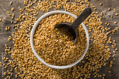 Golden flax seeds in white bow on wooden table. Top view	