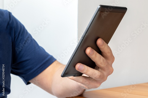 Gray e-reader electronic book in male hand. A man in a blue t-shirt with a tablet. Selective focus