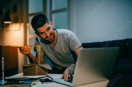 young man working late from his home, eating chinese food