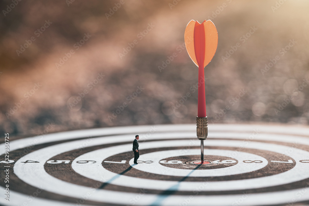 Businessman standing lookup red dart arrow hitting target centre dartboard on sunset background. Business targeting and focus. Businessman standing lookup red dart arrow hitting target centre dartboard on sunset background. Business targeting and focus.