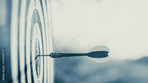 Close up red dart arrow hitting target center dartboard on sunset background. Business targeting and focus concept. photo