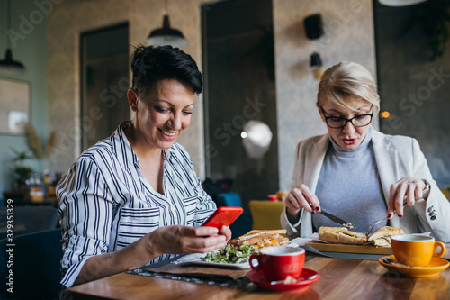 mid aged women using mobile phone while having lunch break with her friend