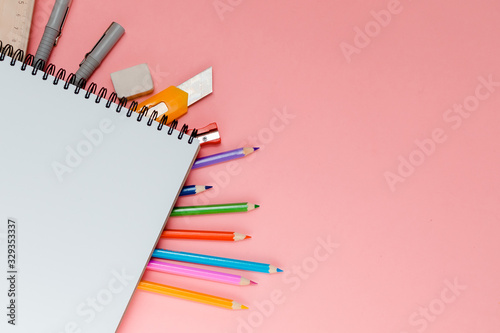 Colorful school supplies under spiral notepad on pink background with place for text. Stationery of different colors. Back to school concept.