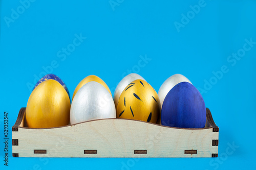 Christ is risen. Easter eggs painted in silver, gold and blue lie in a wooden box. Classic blue background. photo