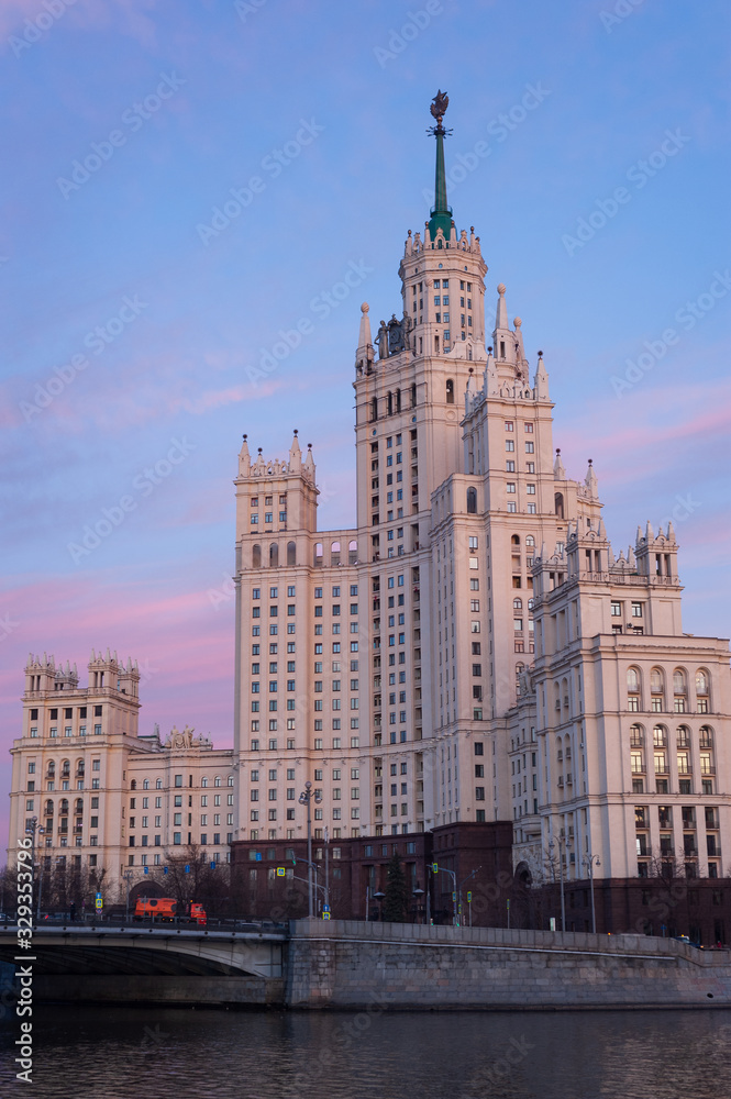 View of illuminated Stalin skyscraper on the Kotelnicheskaya embankment and Moscow River at evening