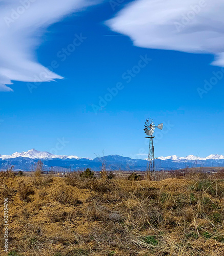 A old fashioned windmill sits atop a grassy hill with blue sky and beautiful clouds.
