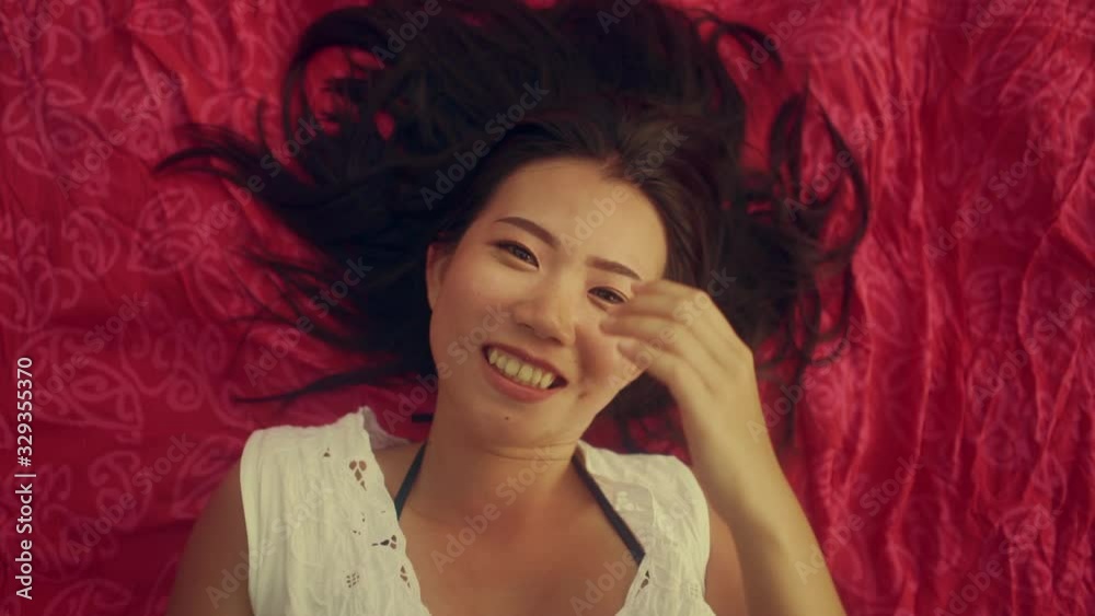 slow motion high angle shot on young beautiful and happy Asian Chinese woman lying flat on sarong smiling cheerful and relaxed and acting sweet in beauty and fashion concept