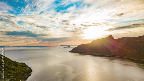 A beautiful sunset on Senja Island. The sun cast its rays down upon the clouds painting them in warm hues of yellow, gold and orange.  Reflection playing on the mirrorlike sea surface. photo