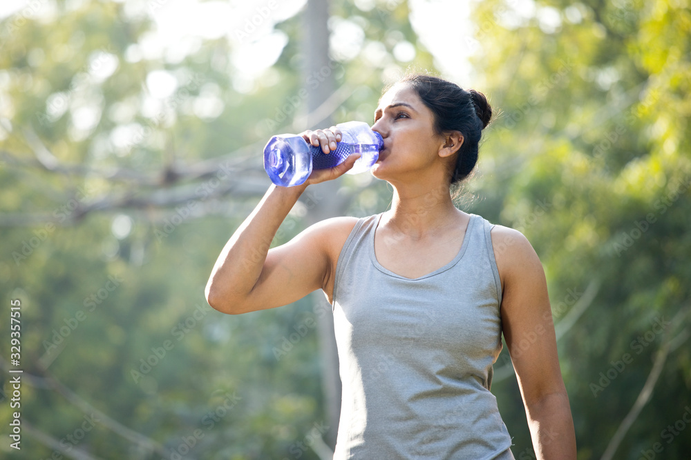 Fit woman with dumbbell shape water bottle at park Fit woman with dumbbell shape water bottle at park