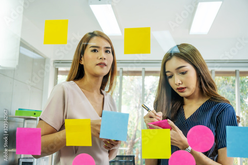 Asian creative business women are writing note on the text sheet after thinking new idea and planning project with colleague ,Group of employee brainstorming idea on glass wall and sticky..