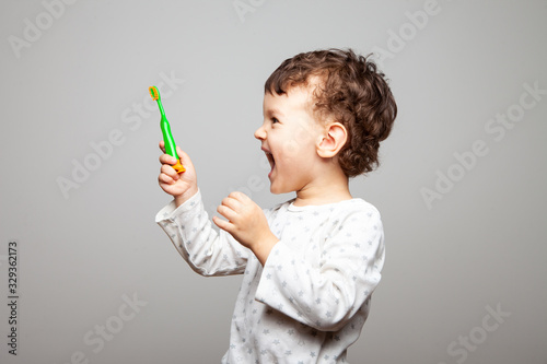 boy looks at a new toothbrush. strong joy, wild delight, a look to the side. hygiene rules. child stands on a gray background, studio, isolated