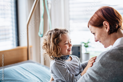 Caring mother visiting small girl daughter in bed in hospital.