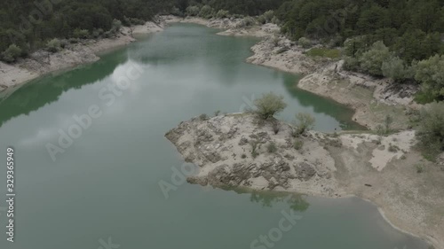 Aerial view of Lake Grahovo in mountains. Beautiful landscape of Montenegro nature. Emerald water of Grahovsko Jezero. Drone flies over lake surface to forest with green trees on hills. Sand and stone