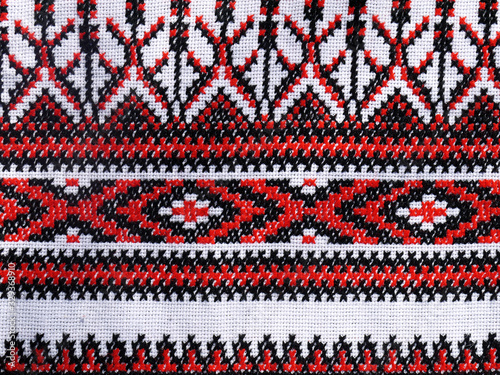 Ukrainian folk hand embroidery. Embroidered ornament with red-black threads on white fabric.