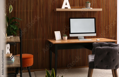 Comfortable workplace with computer near wooden wall in stylish room interior. Home office design © New Africa