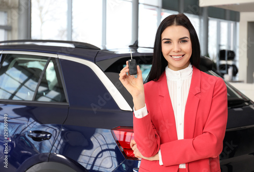 Saleswoman with key near car in dealership