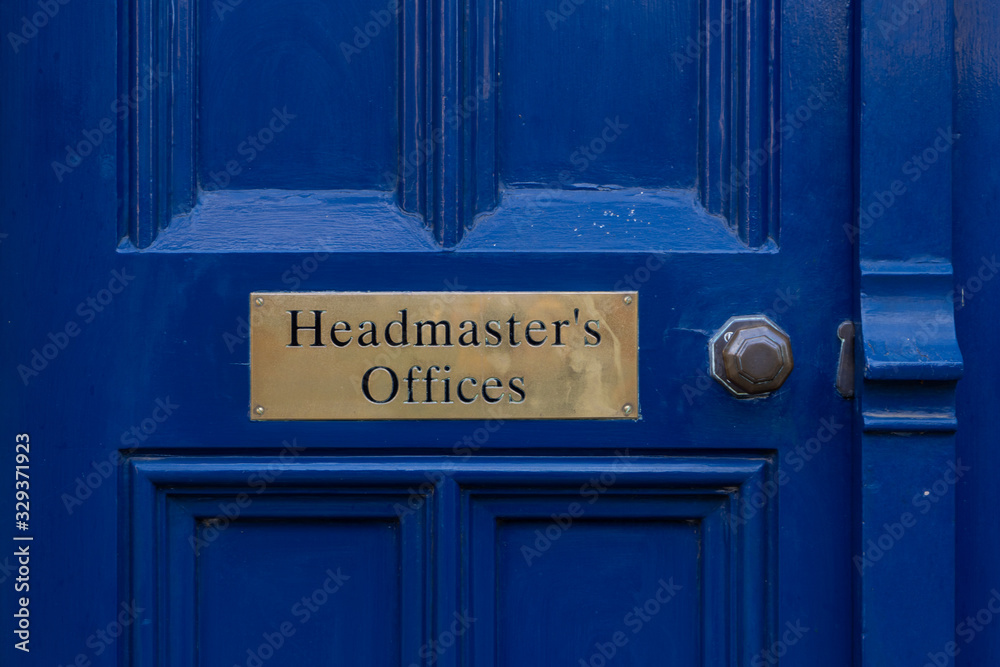 A brass sign reading Headmasters offices on a old blue door with a brass handle A brass sign reading Headmasters offices on a old blue door with a brass handle