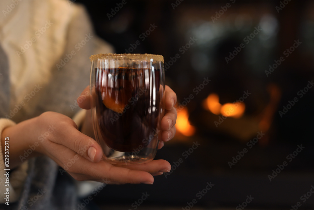 Woman with tasty mulled wine near fireplace indoors, closeup