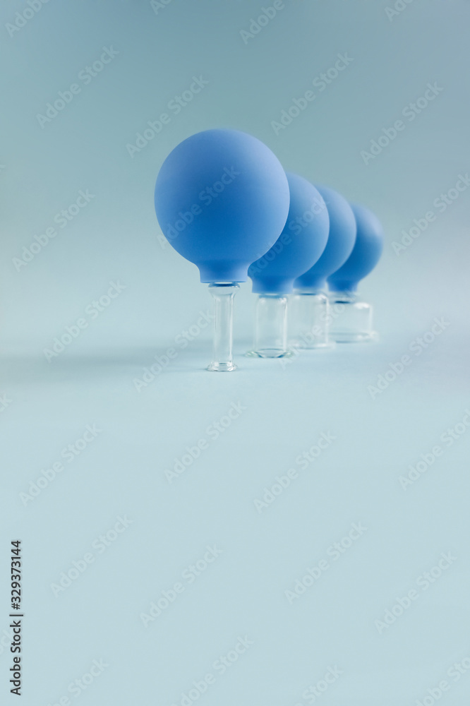 Vacuum cans stand behind each other in soft focus. Vertical photo of glass jars for facial massage.