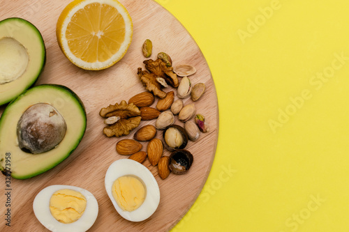 Flat lay ketogenic diet.   vocado eggs lemon nuts on the wooden cutting board on the yellow background. Concept of healthy food.Copy space for mock up