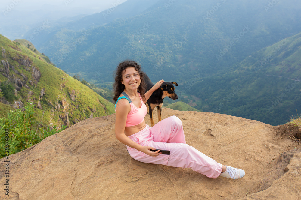 A girl with a dog enjoying the mountain scenery on the edge of a cliff